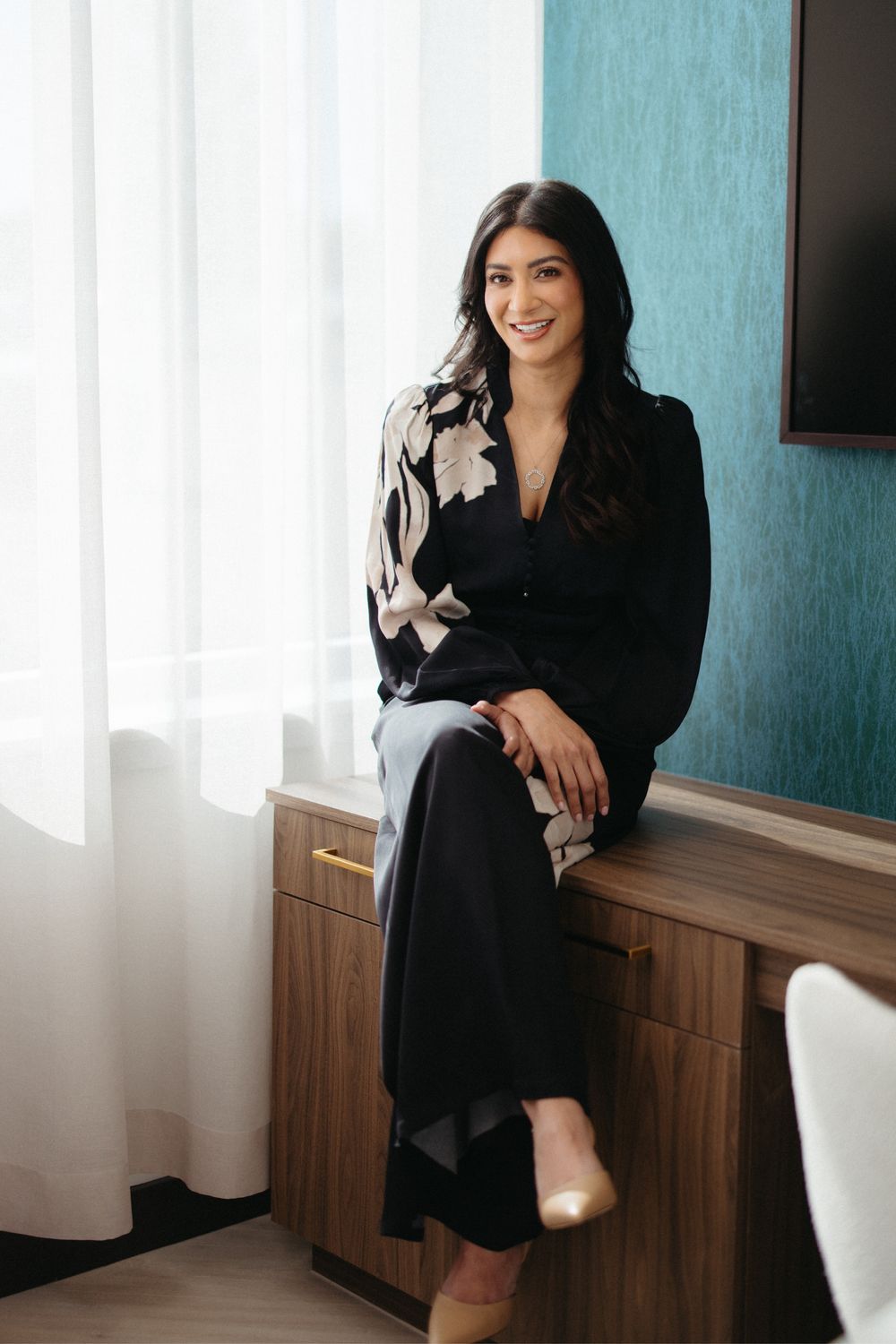 Smiling woman in stylish outfit, seated indoors.