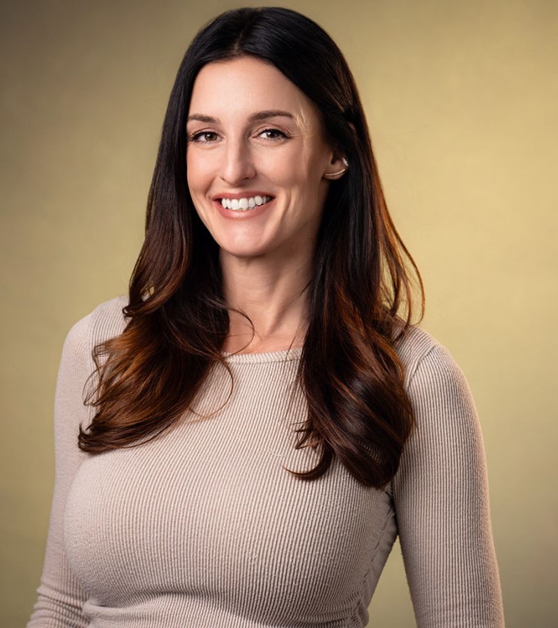Smiling woman with long hair in a beige top.