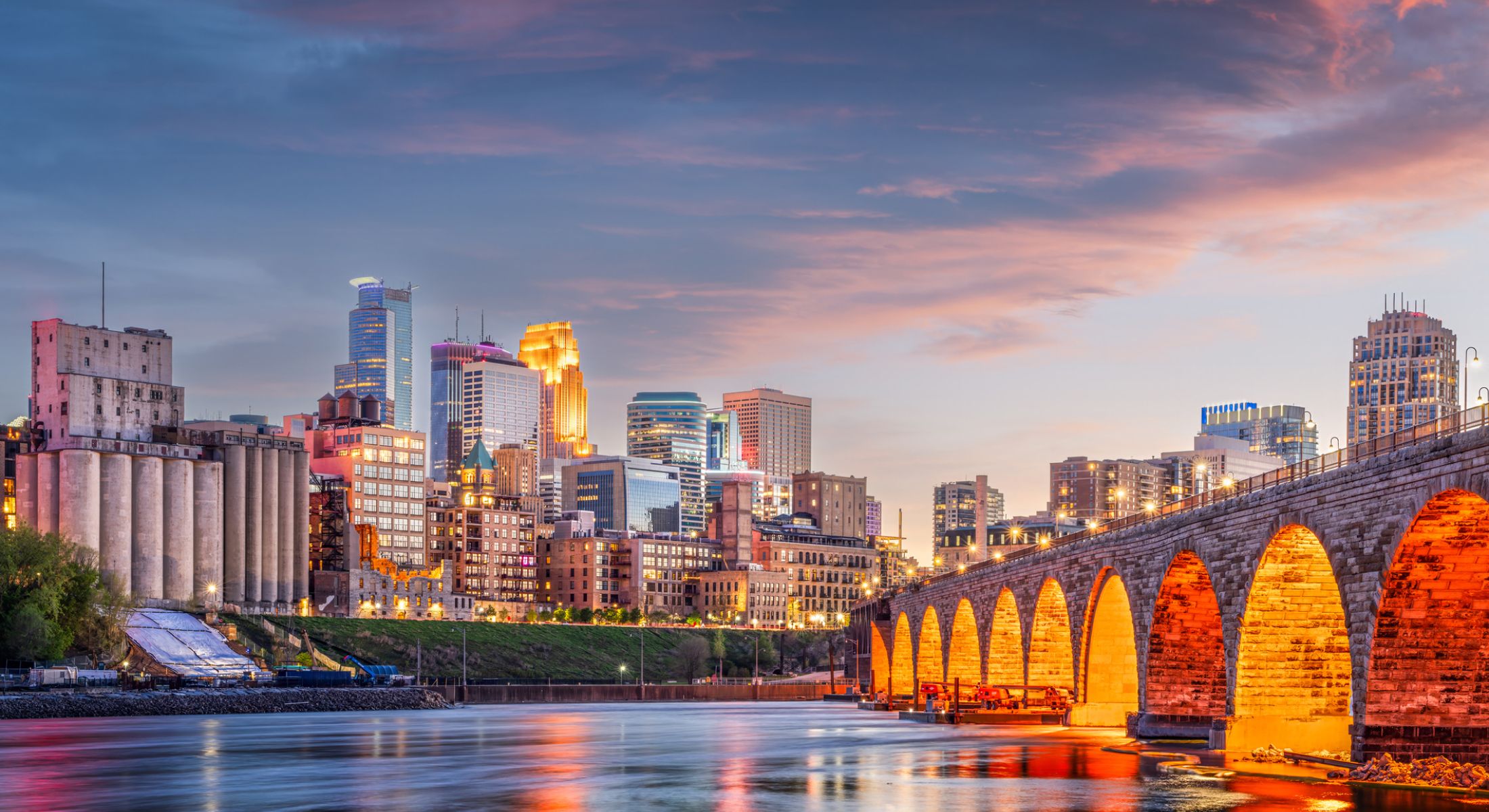 Minneapolis skyline at sunset with stone bridge.