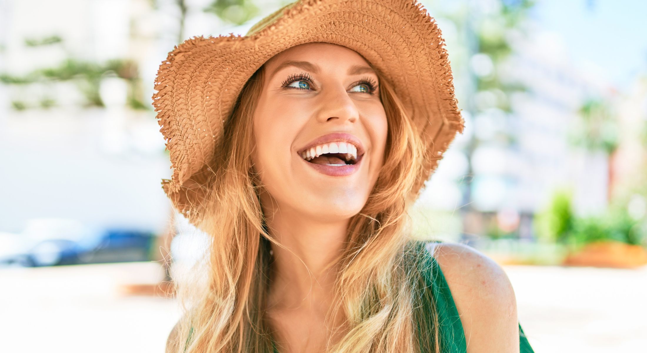 Smiling woman wearing a straw hat outdoors.