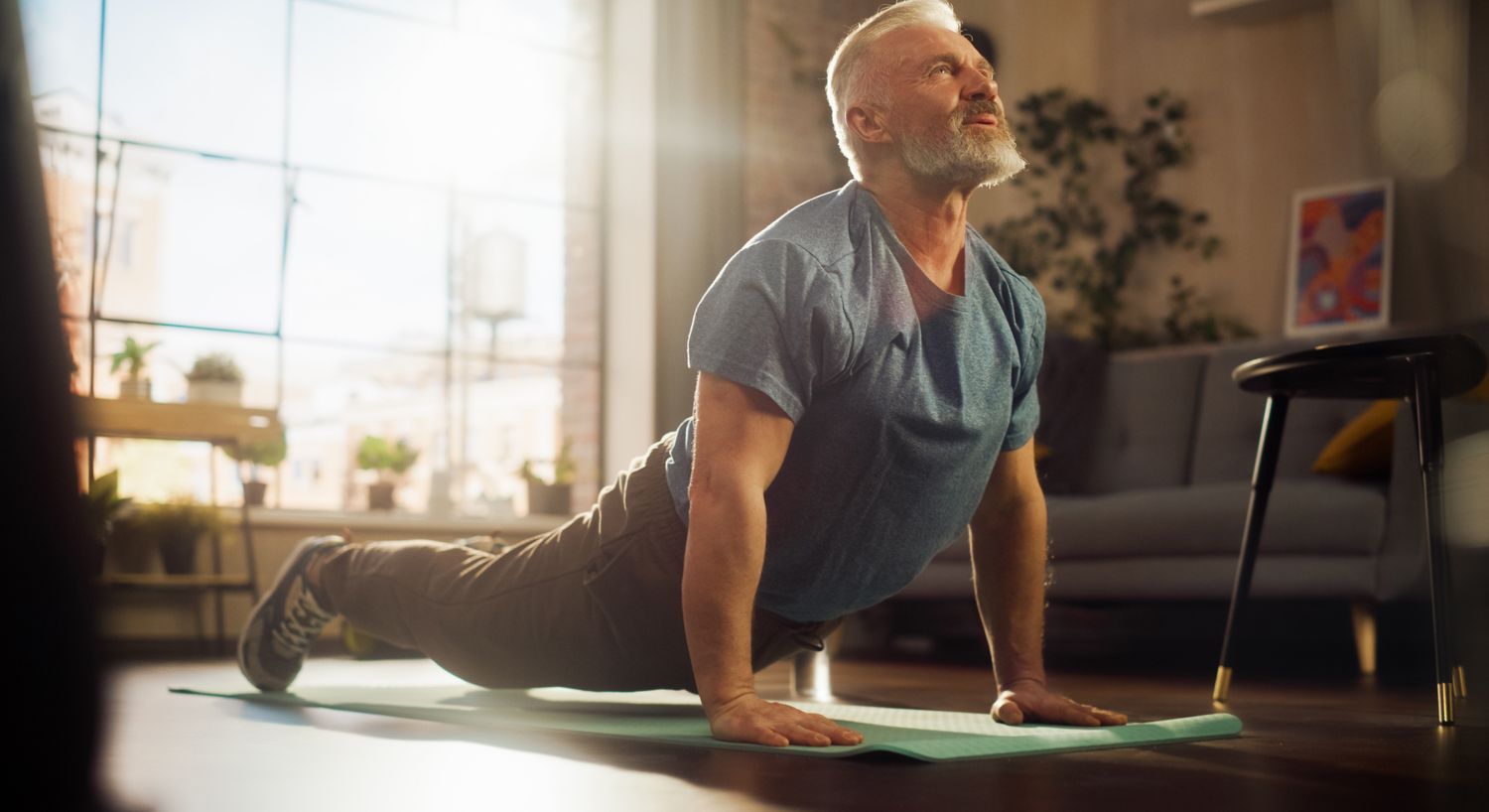 Older man practicing yoga in sunlit room.